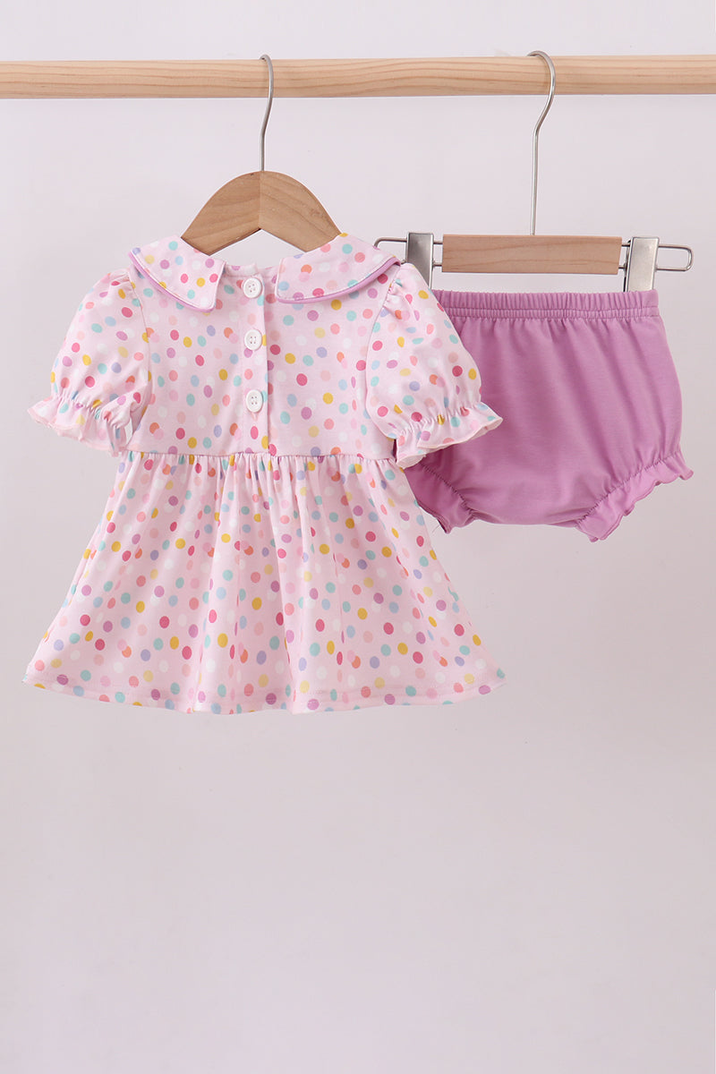 Baby girl's outfit with polka dot dress and pink bloomers on a hanger against a white background