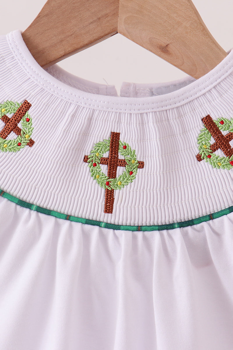 White dress with green trim and red embroidery on a hanger against a beige background
